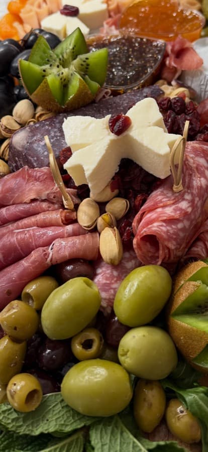 A close-up of star-shaped cheese, olives, salami, and pistachios on a Maison board